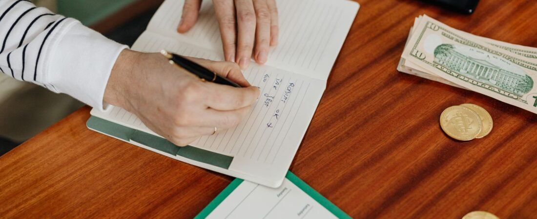 Writing a plan in a notebook beside cash and a phone to set up the best free budgeting app 2026.