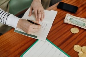 Writing a plan in a notebook beside cash and a phone to set up the best free budgeting app 2026.