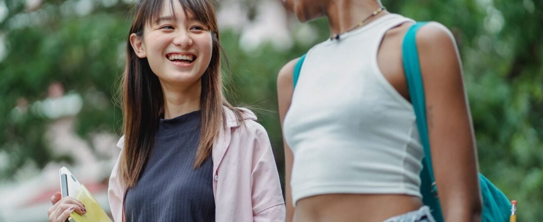 Two happy college girls laughing together on campus, one holding a laptop from her college tech kit