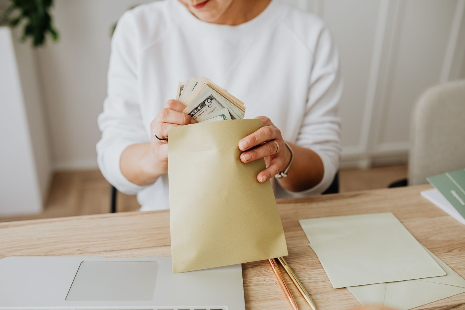 A person putting cash into a labeled envelope for envelope-style budgeting at a bright desk.