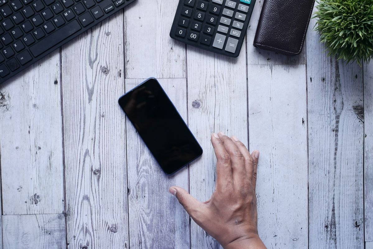 A hand reaching for a phone on a desk, the reflex screen time apps aim to interrupt