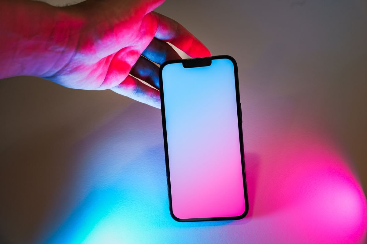 A smartphone glowing with pink and blue light, held in one hand