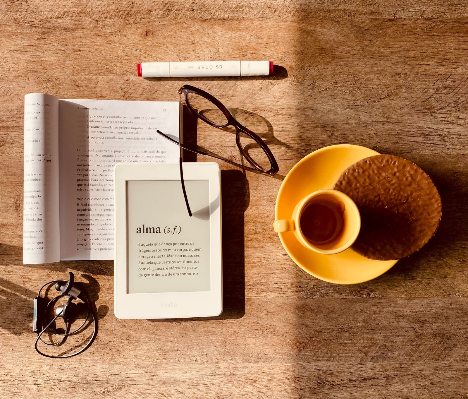 E-reader with earphones, coffee and a book on a table