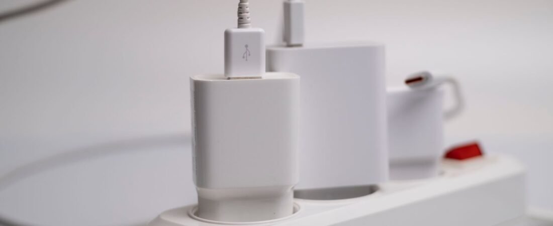 White power strip with chargers plugged in, the standby devices a smart plug can switch off to cut vampire power.