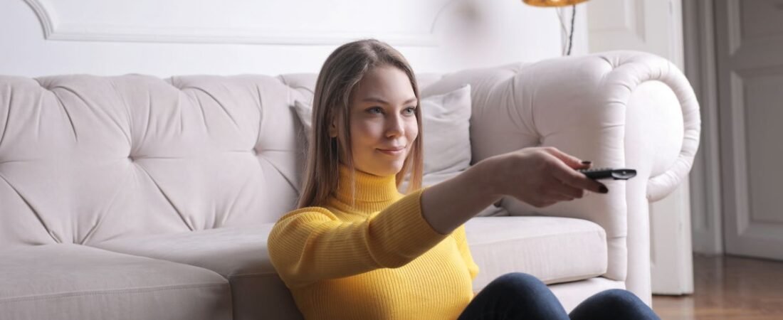 Person in a bright living room pointing a TV remote to choose a streaming service