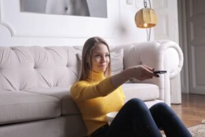 Person in a bright living room pointing a TV remote to choose a streaming service