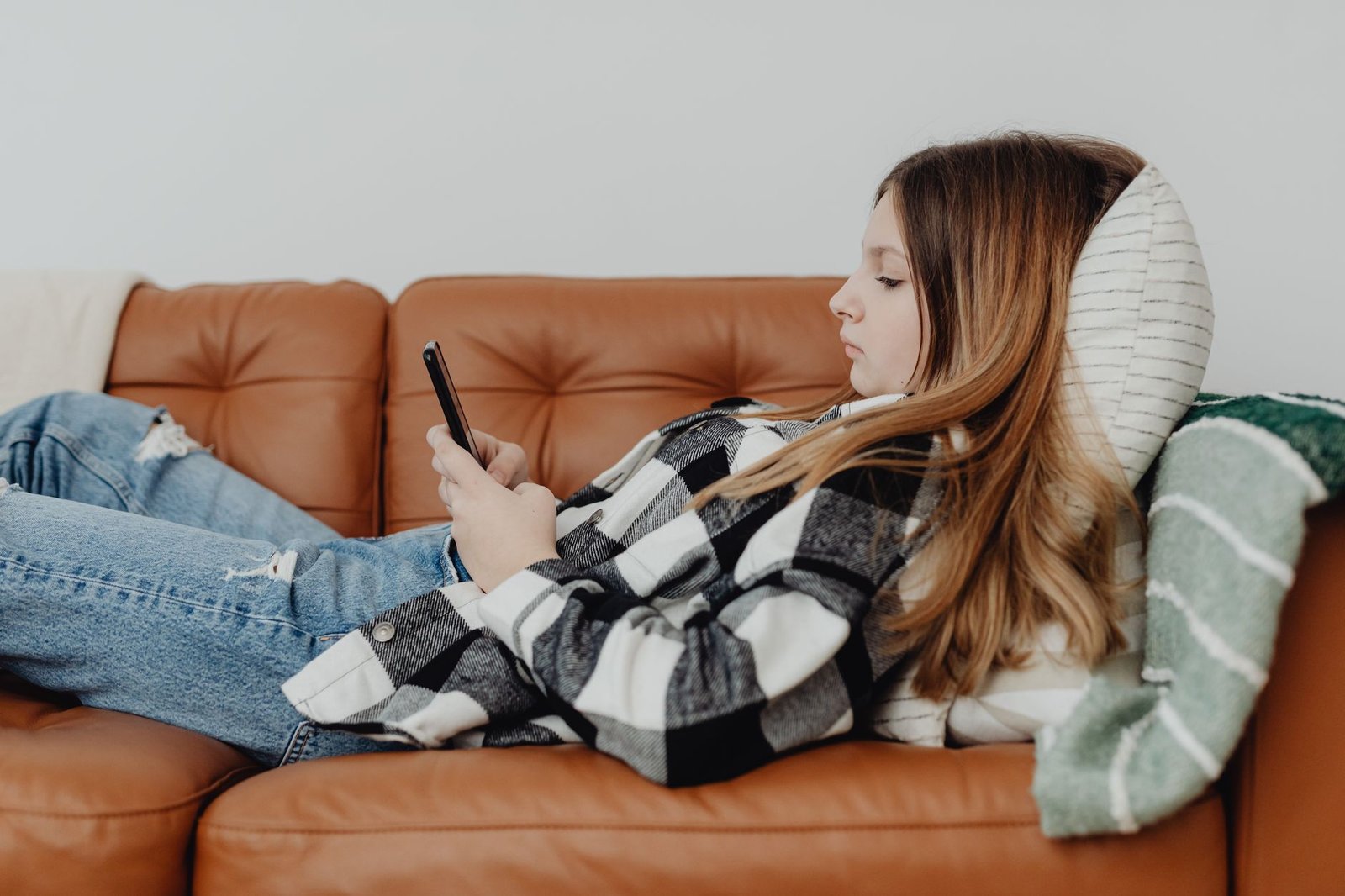 Teenager using a phone on a couch while a parent sits nearby