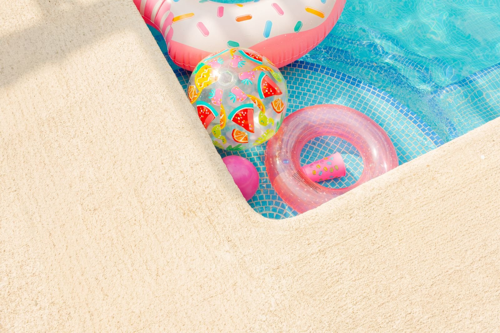 Colorful inflatable floats in a bright blue swimming pool on a sunny summer day.