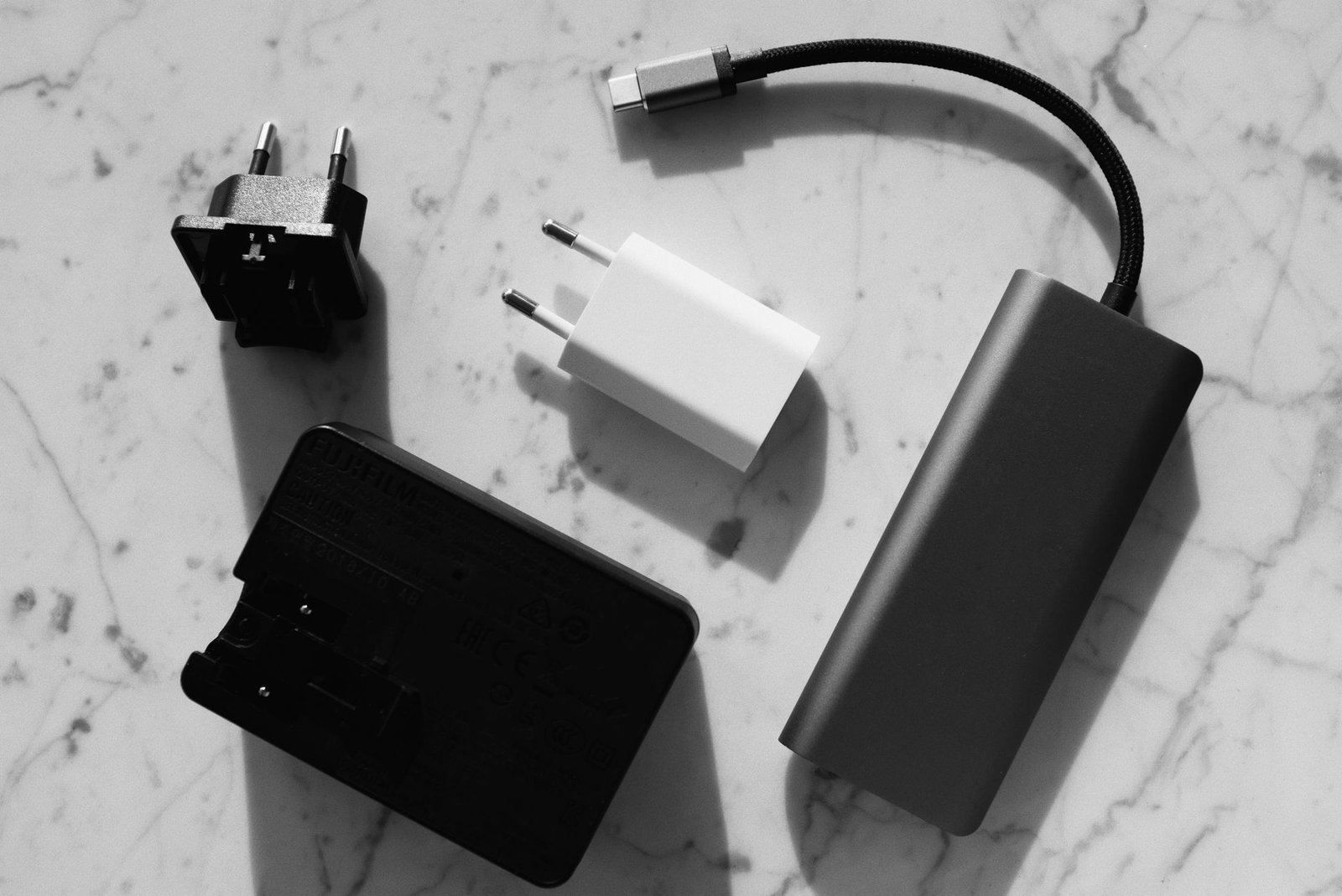 A small white USB-C GaN charger beside bulkier old power adapters and a power bank.
