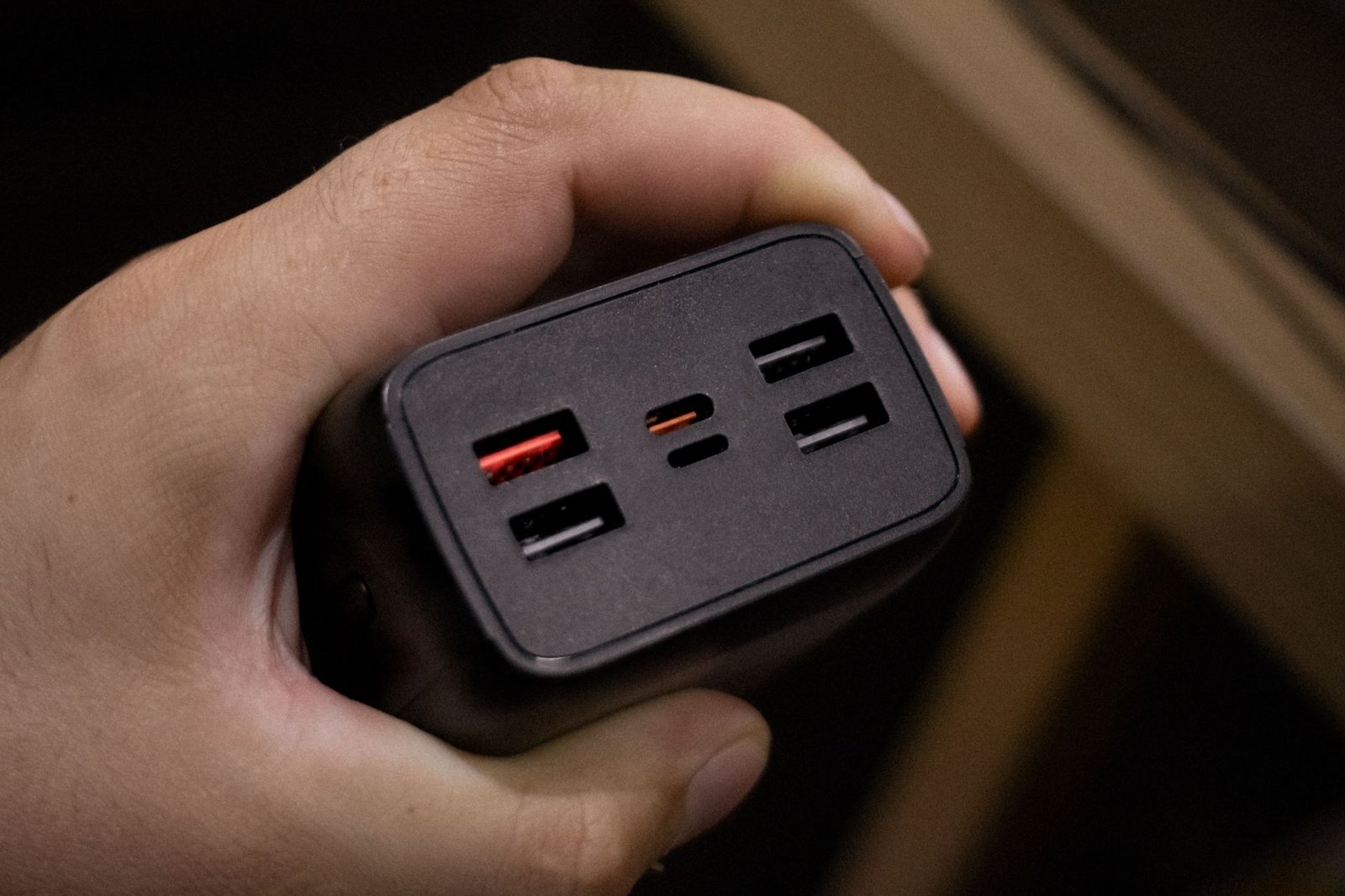 A hand holding a compact multi-port USB charger, showing its USB-C and USB-A ports.