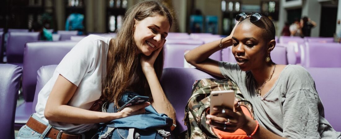 Two travelers checking smartphones on public wifi in a bright airport terminal