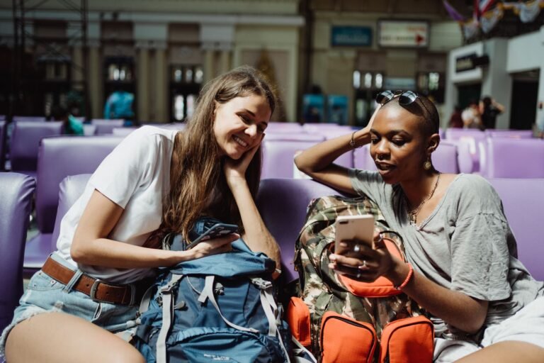 Two travelers checking smartphones on public wifi in a bright airport terminal