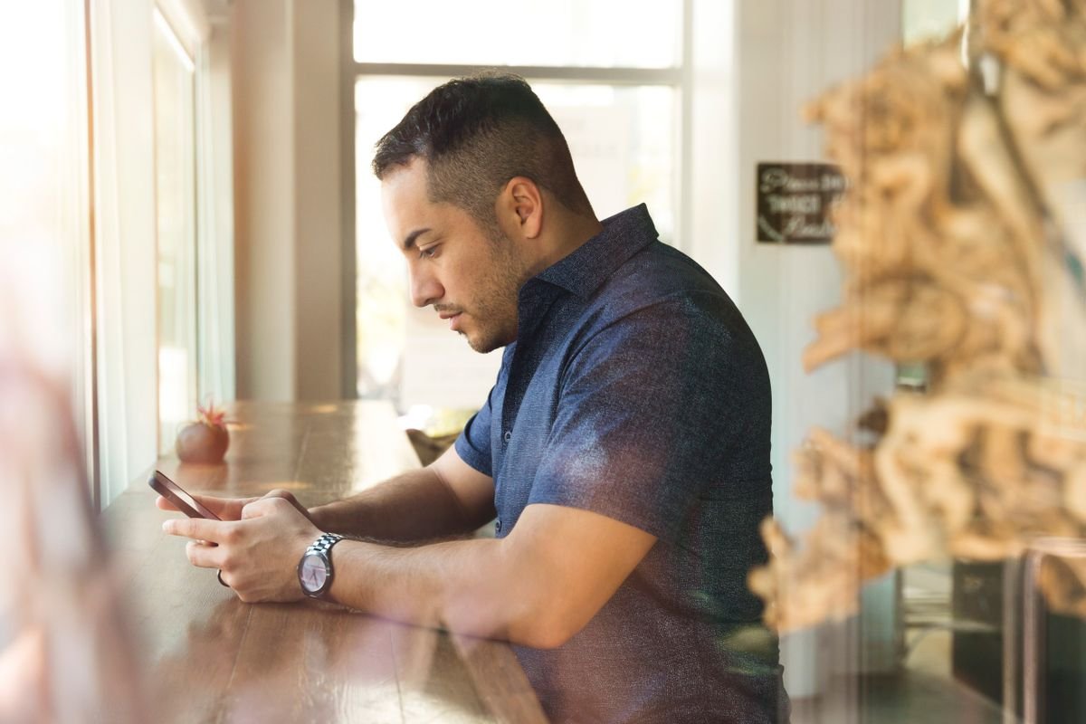 A man checking his phone at a cafe while weighing whether to upgrade now or wait