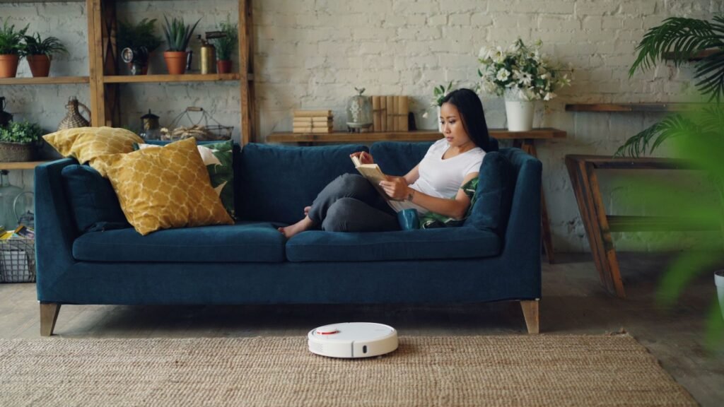 Robot vacuum cleaning a bright, cozy living room while a person relaxes on the sofa.