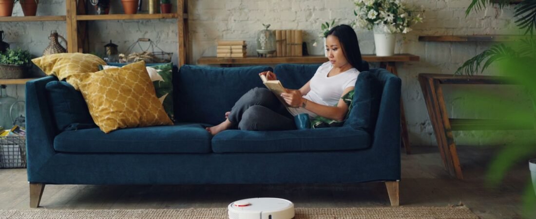 Robot vacuum cleaning a bright, cozy living room while a person relaxes on the sofa.