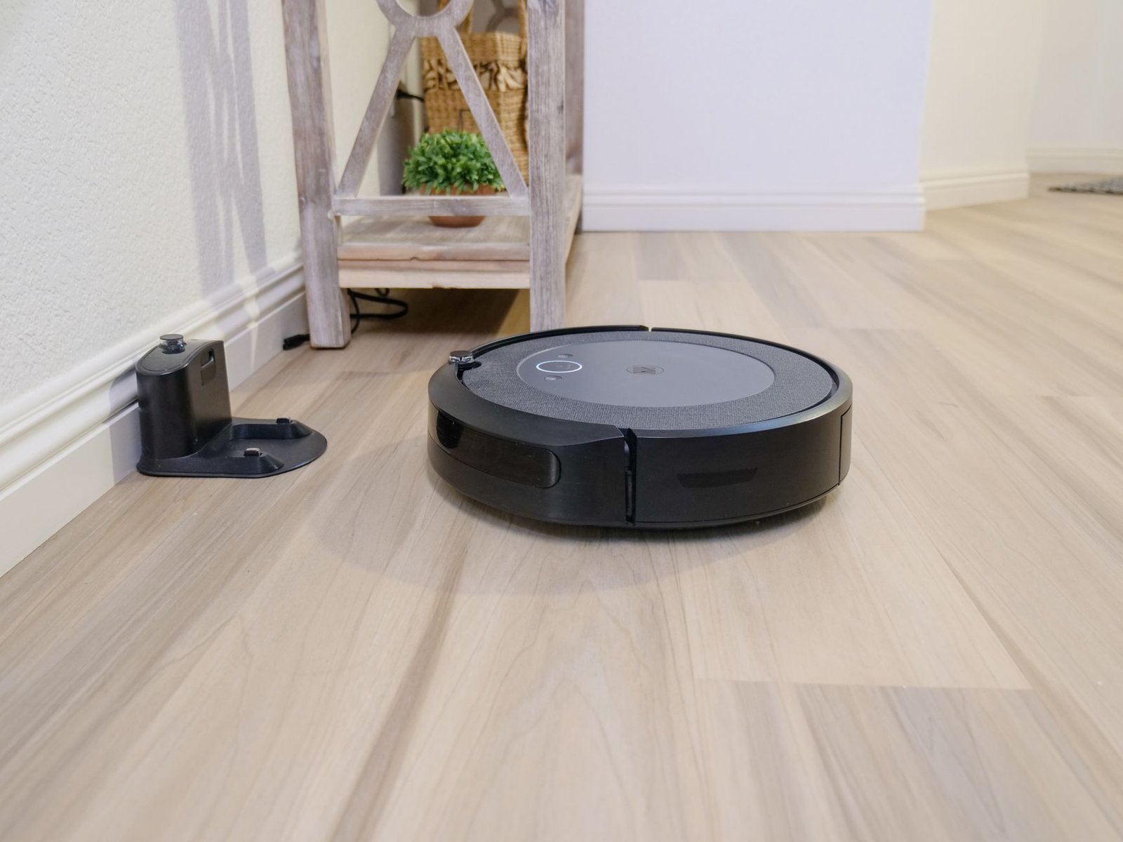 Robot vacuum returning to its charging and docking station on a light wood floor.